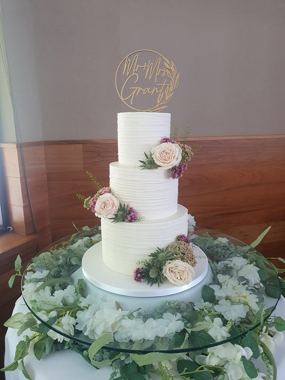White three-tier cake with light pink roses and gold circular cake topper